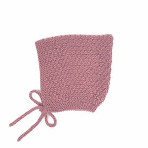 Può includere: Un cappuccio lavorato a maglia di colore rosa antico. Il cappuccio ha un motivo a punto strutturato e si lega al mento con due cordoncini lavorati a maglia. Il cappuccio è progettato per coprire la testa e il collo.