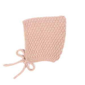 May include: A pale pink knitted baby bonnet with a tied bow at the bottom.