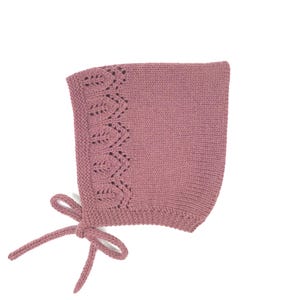 Può includere: Un cappuccio per neonati lavorato a maglia color rosa antico con un motivo decorativo a foglie sul bordo. Il cappuccio ha una chiusura con fiocco ed è realizzato in filato morbido e strutturato. Un accessorio affascinante per neonati.
