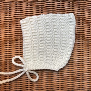 May include: A white crocheted baby bonnet with a tied bow.