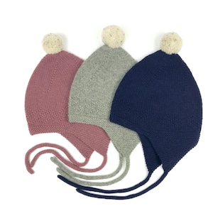 Può includere: Tre cappellini di lana per neonati con pon pon. I cappellini sono rosa, grigio e blu scuro.