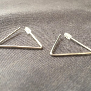Puede incluir: Un par de pendientes triangulares de plata con postes de plástico transparente.