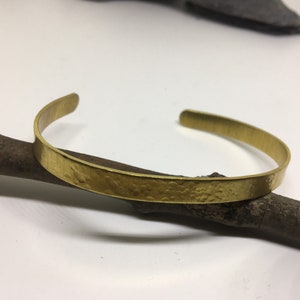 May include: A gold-toned hammered metal bracelet. The bracelet is simple and minimalist, with a smooth, rounded finish.