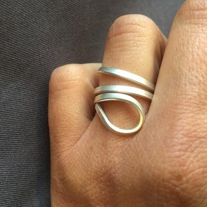 Puede incluir: Un anillo de plata con un diseño único y retorcido. El anillo está hecho de múltiples bandas de plata que se entrelazan para crear una forma fluida y orgánica.