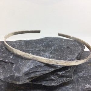 May include: A silver bangle bracelet with a hammered finish. The bracelet is simple and elegant, and would make a great gift.