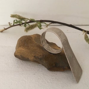 May include: A silver ring with a unique, curved design. The ring is resting on a brown rock.