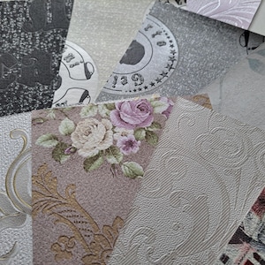 May include: A collection of overlapping wallpaper samples featuring diverse textures and patterns, including floral motifs with pink roses, embossed scrollwork, metallic gold accents, and monochromatic graphic prints with circular text elements.