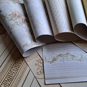 May include: A selection of wallpaper rolls in diverse patterns and colours. Some rolls are unrolled, displaying floral, striped, and textured designs. Colours include cream, beige, and touches of pink and green. Suitable for home decor projects.