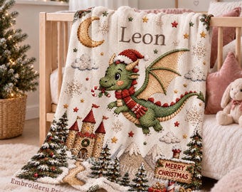 May include: A cream-colored fleece blanket featuring a green dragon wearing a Santa hat and scarf, a castle, a crescent moon, and snowflakes. The text "Leon" and "Merry Christmas" are printed on the fabric, which has an embroidery print look.