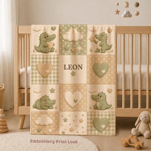 Pode incluir: Uma manta de bebé com design de patchwork em tons de verde sálvia, creme e bege. A manta apresenta ilustrações de crocodilos verdes, corações, nuvens e estrelas. O nome LEON está impresso no quadrado central em letras castanho-escuras.