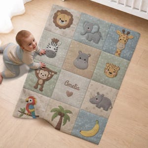 Könnte beinhalten: Babydecke mit Patchwork-Design und Applikationen von Tieren wie Löwe, Elefant, Zebra, Giraffe, Nilpferd, Leopard, Affe, Papagei, Nashorn, Palme und Banane. Der Name "Amelia" ist auf die Decke gestickt.