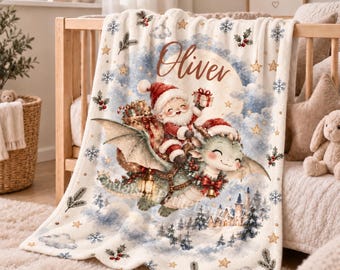 May include: A cream-colored fleece blanket featuring a festive illustration of Santa Claus riding a green dragon. The design includes the name Oliver, a snowy village, holly, snowflakes, and gold stars. The blanket has a soft texture and a printed pattern.