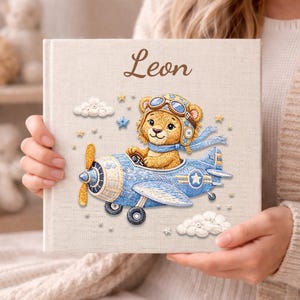 May include: A personalized children's book with the name "Leon" on the cover. The cover features a cartoon bear wearing a pilot's hat and scarf, seated in a blue airplane. The design includes clouds, stars, and a propeller.