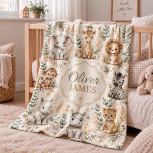 May include: A cream-colored fleece blanket featuring a central decorative frame with the text Oliver James. The blanket is decorated with illustrations of a baby elephant, giraffe, lion, monkey, zebra, rhino, and leopard, surrounded by green leaves.