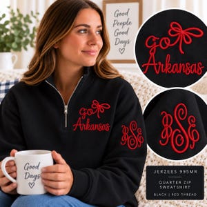 May include: A black quarter-zip sweatshirt featuring red embroidered text that reads "go Arkansas" with a bow graphic on the chest and a red embroidered monogram on the sleeve. The sweatshirt is labeled Jerzees 995MR and uses red thread.