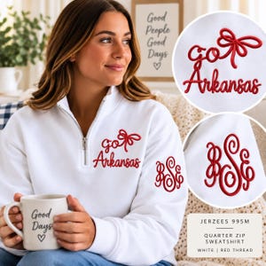 May include: A white quarter-zip sweatshirt featuring red embroidery on the chest that reads "go Arkansas" with a bow icon. The left sleeve displays a red embroidered monogram with the letters "BSE". The fabric is a Jerzees 995M style.