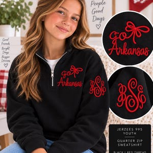 May include: A black quarter-zip sweatshirt featuring red embroidery. The chest displays the text "go Arkansas" with a bow graphic, while the sleeve features a red monogram with the letters "BSE". The garment is labeled as Jerzees 995 Youth.