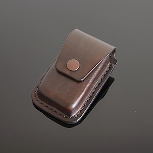 May include: A brown leather case with a copper button closure. The case is designed to hold a small item, such as a lighter or a pocket knife.