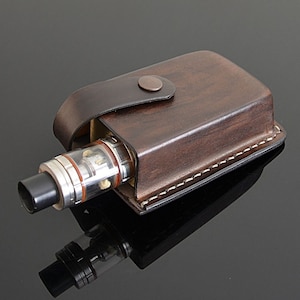 May include: A brown leather case with a stitched edge and a flap closure. The case is designed to hold a vape pen, which is partially visible inside the case.