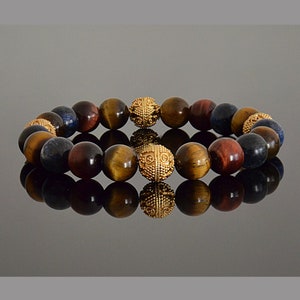 Op de afbeelding: Een veelkleurige kralen armband met gouden accenten. De armband is gemaakt van tijgeroog, rood tijgeroog en blauwe lapis lazuli kralen.