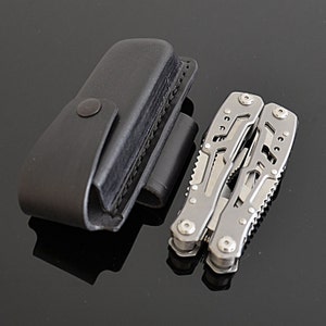 Peut inclure: Un outil multifonction en acier inoxydable, avec plusieurs outils et un &eacute;tui en cuir noir avec une fermeture &agrave; bouton-pression. L'outil multifonction est ouvert, montrant ses composants. L'&eacute;tui est ferm&eacute;.