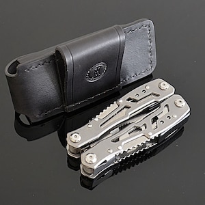 Peut inclure: Un outil multifonction en acier inoxydable avec divers instruments, &agrave; c&ocirc;t&eacute; d'un &eacute;tui en cuir noir. L'outil multifonction est ouvert, affichant ses composants. L'&eacute;tui porte un logo estamp&eacute;.