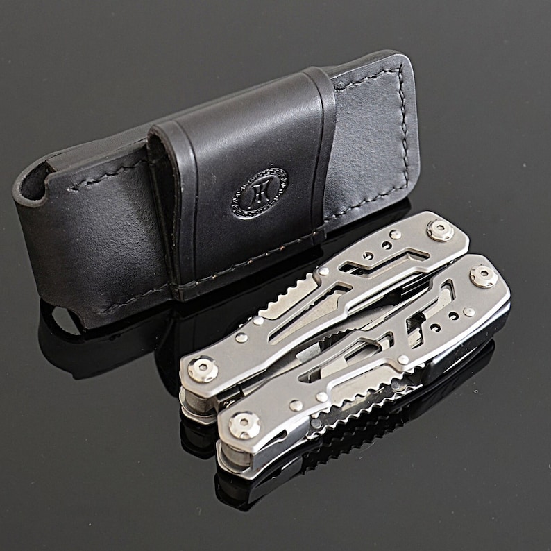 Peut inclure: Un outil multifonction en acier inoxydable avec divers instruments, &agrave; c&ocirc;t&eacute; d'un &eacute;tui en cuir noir. L'outil multifonction est ouvert, affichant ses composants. L'&eacute;tui porte un logo estamp&eacute;.