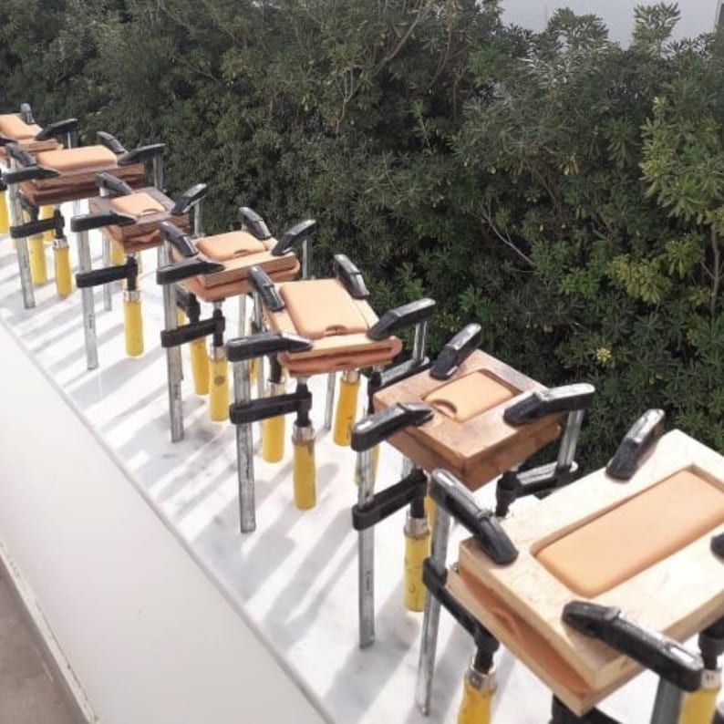 Puede incluir: Una fila de marcos de madera con inserciones naranjas se sujetan con abrazaderas met&aacute;licas. Las abrazaderas est&aacute;n aseguradas con manijas amarillas.