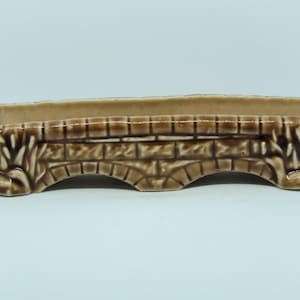 May include: A brown ceramic planter shaped like a bridge with arched openings. The planter has a textured surface and is decorated with a brick pattern.