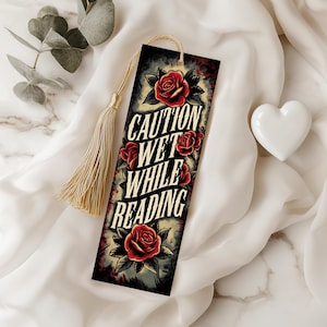 Pode incluir: Um marcador de página com fundo preto e rosas vermelhas. O texto no marcador de página diz "Caution Wet While Reading".