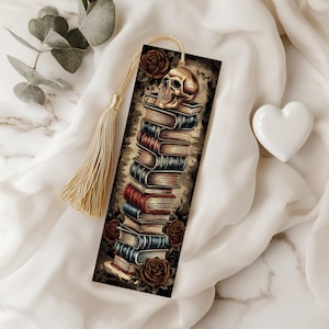 May include: A gold bookmark with a tassel features a stack of books with a skull on top. The bookmark has a dark background with red and white roses.