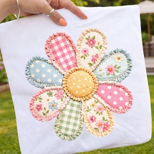 May include: A white pillowcase featuring a large, appliqued flower. The flower has eight petals in various patterns, including polka dots, gingham, and floral prints. The center is yellow with white polka dots. The petals are outlined with a ruffled edge.
