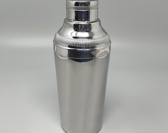 Puede incluir: Un coctelera de plata con un acabado liso y pulido. La coctelera tiene una parte superior redondeada y un cuerpo cilíndrico.