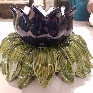 May include: A ceramic lotus flower-shaped decorative piece. The top is a deep blue, flower-shaped bowl with a white interior. The base is a green, leaf-shaped design. The piece is likely used for decorative purposes.