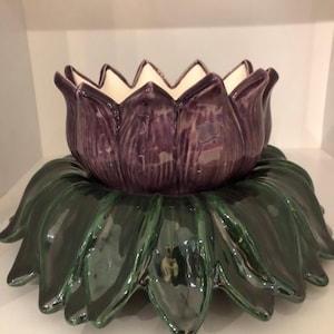 May include: A purple ceramic flower pot with a green leaf base. The pot is shaped like a flower with a white interior.