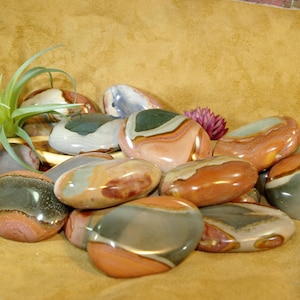 May include: A collection of polished, multi-colored, banded agate stones. The stones are smooth and oval-shaped, with shades of brown, gray, and white.