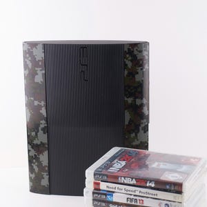 Puede incluir: Una consola PlayStation 3 de color negro y verde camuflaje con una pila de videojuegos que incluyen NBA 2K14, Need for Speed ProStreet, FIFA 13, God of War: Ascension, Killzone 2, Call of Duty: World at War y Call of Duty: Modern Warfare 2.