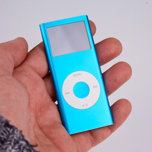 May include: A turquoise digital media player with a screen and a circular control pad. The control pad has a white center with a blue circle and directional buttons. The word "MENU" is above the control pad.