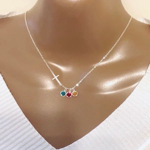 May include: A silver chain necklace with a small cross charm and three dangling round gemstones. The gemstones are teal, yellow, and red.