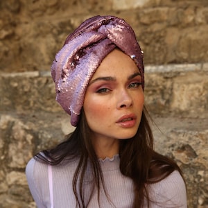 May include: A pink sequined turban with a knot on top. The turban is made of a soft, sparkly fabric.