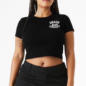 Puede incluir: Top corto negro con el texto blanco "SMASH your GLASSES". La camiseta tiene mangas cortas y cuello redondo. La modelo lleva pantalones a rayas blancas y negras.