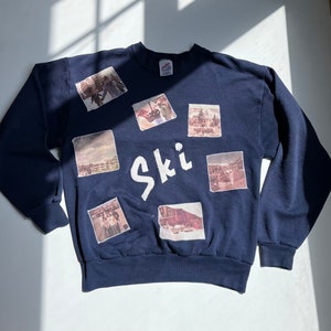 May include: A navy blue sweatshirt with a white "Ski" graphic and multiple vintage photos of people and landscapes sewn onto the front.