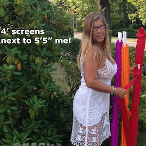 May include: A woman in a white lace dress stands next to four colorful screens. The screens are red, orange, and purple. The text on the image says "4' screens next to 5'5" me!"