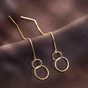 May include: A pair of gold dangle earrings with two connected circles. The circles are slightly textured and the earrings have a delicate chain.