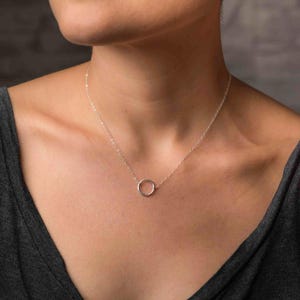Könnte beinhalten: Eine silberne Halskette mit einem schlichten Kreisanhänger. Die Halskette ist zart und minimalistisch und somit ein perfektes Accessoire für jeden Tag.