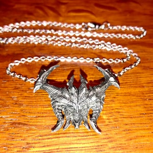May include: A silver necklace with a detailed, demonic-looking pendant. The pendant is shaped like a skull with horns and sharp teeth.