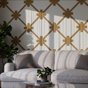May include: A living room scene featuring a white sofa with two patterned throw pillows. A glass coffee table holds a small potted plant. The wall has a gold geometric pattern. A large potted plant is on the left.