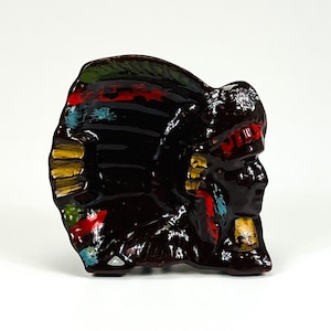 May include: A ceramic figurine of a Native American chief wearing a headdress with colourful feathers. The figurine is painted in shades of brown, red, yellow, green, and blue.