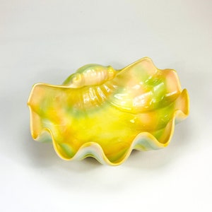May include: A yellow, green, and pink ceramic bowl shaped like a seashell. The bowl has a wavy edge and a smooth, glossy finish.
