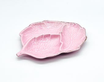 Può includere: Un piatto da portata in ceramica rosa a forma di foglia con tre sezioni. Il piatto ha un motivo a foglia bianca e un bordo dorato.
